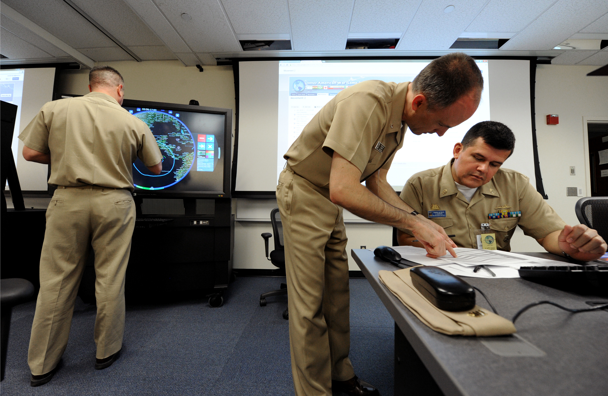 130509-N-PX557-055 (May 9, 2013) NEWPORT, R.I. Commander Keith Powell (center), assigned to U.S. Naval War College (NWC) war gaming department, and Colombian navy Capt. Jamie Garcia, from Escuela Superior de Guerra, collaborate together as Cdr. Dustin Martin (left), assigned to NWC war gaming department, provides inputs to a multi-touch multi-user interface as part of a control group at NWC in Newport, R.I. during the 2013 Inter-American War Game. The 2013 Inter-American War Game is a multinational online war game scenario facilitated through the hosting country’s control group. Control group members are responsible for oversight of the war gaming operations and provide face-to-face analysis, interpersonal discussion and feedback as the scenarios are executed. Multi-touch multi-user interfaces allow control group members to visually depict war gaming player movements for analysis and adjudication. (U.S. Navy photo by Chief Mass Communication Specialist James E. Foehl/Released)